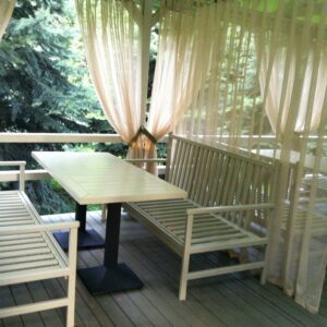 A cream table and benches behind translucent curtains on the terrace - the comfort of Wood Luxury.